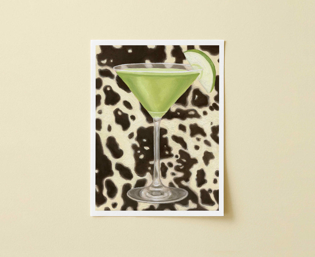 Print of green cocktail in a martini glass with an apple wedge on a black and white cow patterned background