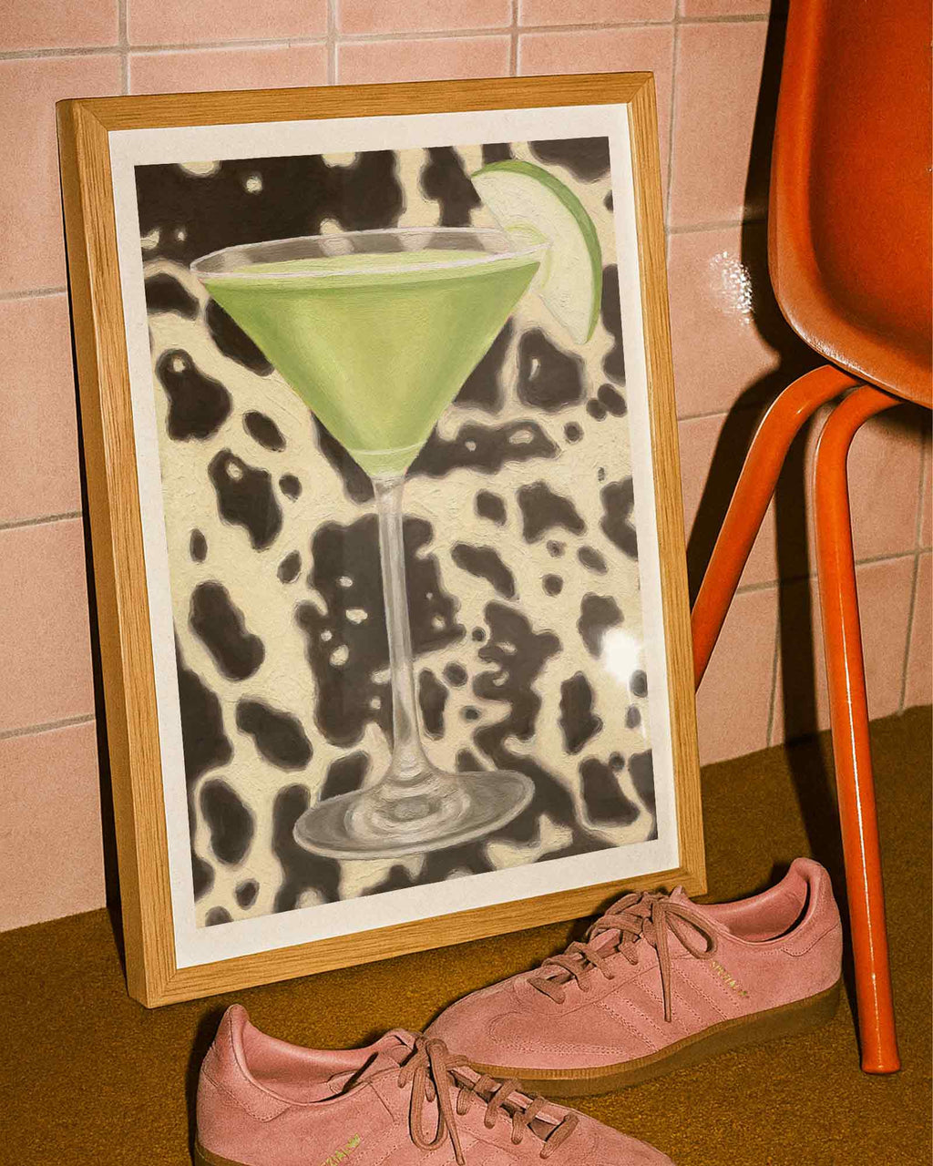Framed artwork of a green cocktail with a cow print background next to pink sneakers.