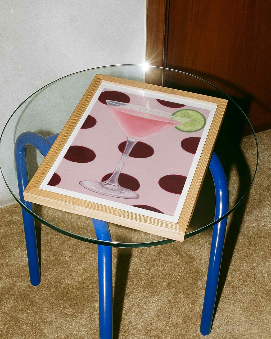 Glass table with a framed picture of a cocktail on a carpeted floor.