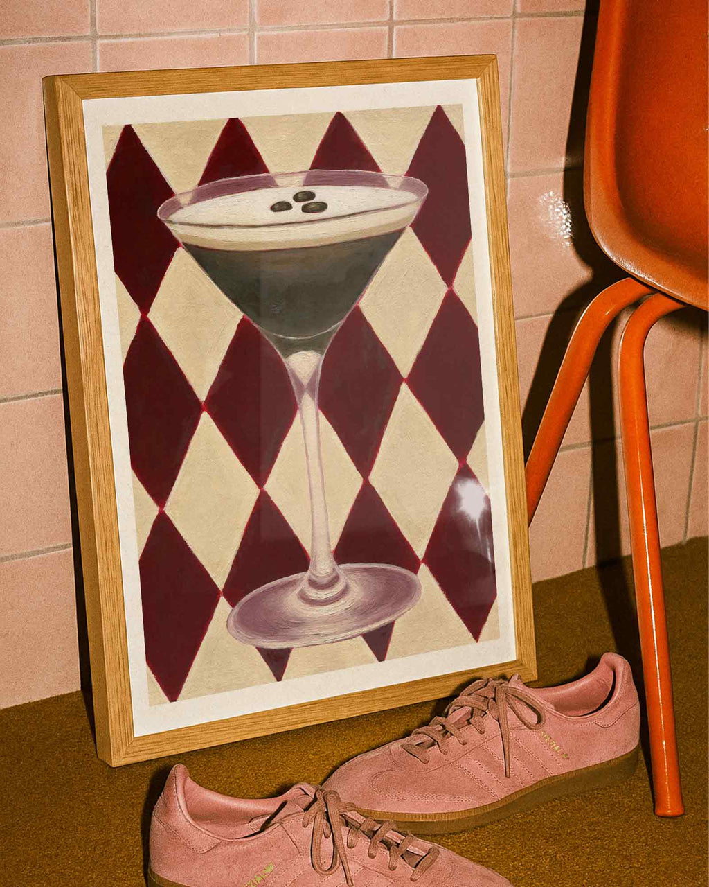Framed artwork of a cocktail with a checkered pattern on a wall next to pink shoes and an orange chair.