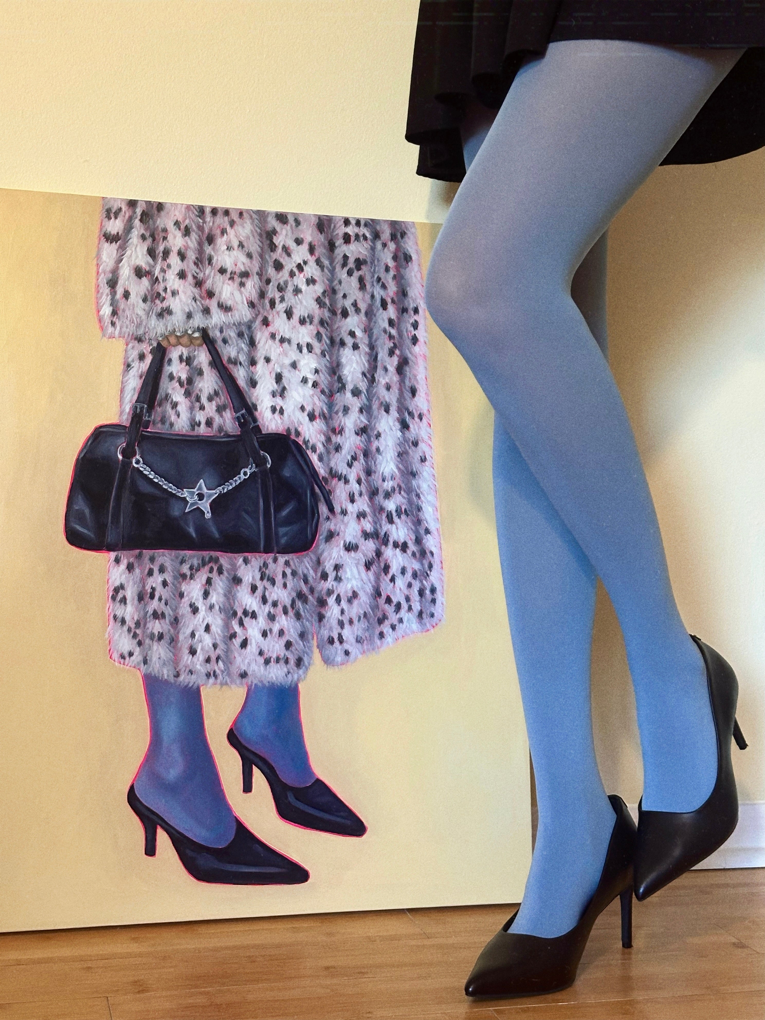 Woman wearing blue tights with black heels, standing next to painting of a fur coat, blue tights, black heels, black bag.
