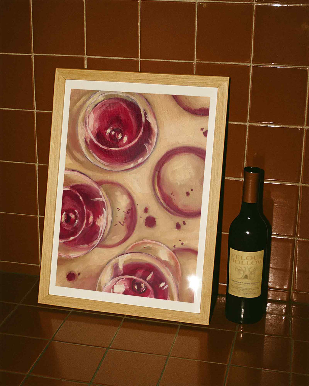Framed artwork of wine glasses on a tiled wall next to a bottle of wine.