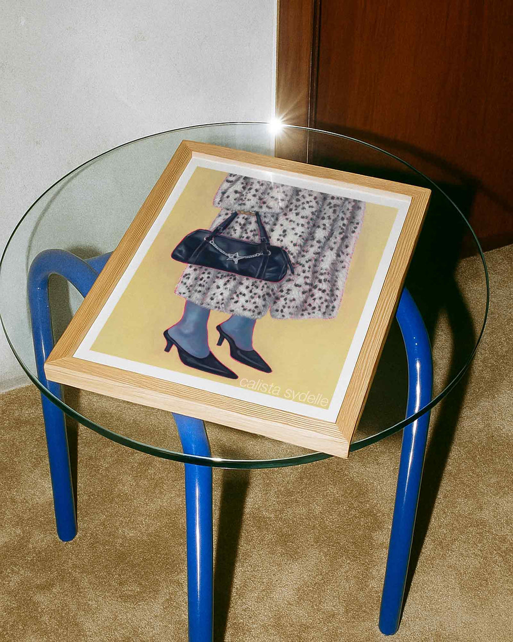 Framed artwork on a glass table with blue metal legs