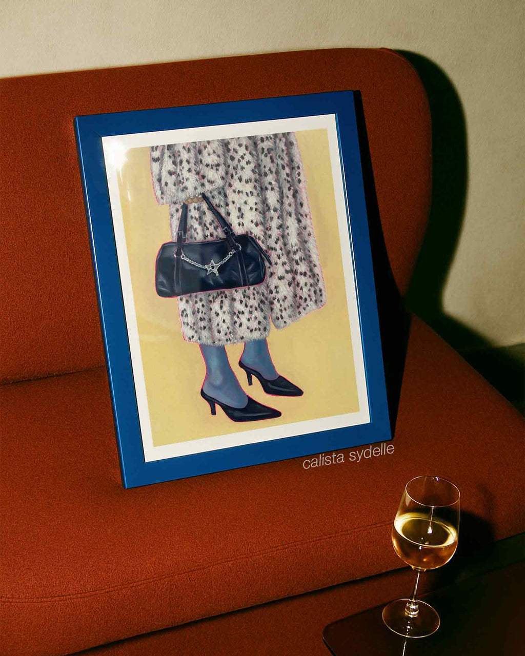 Framed artwork of a person in a fur coat with a handbag on an orange couch.