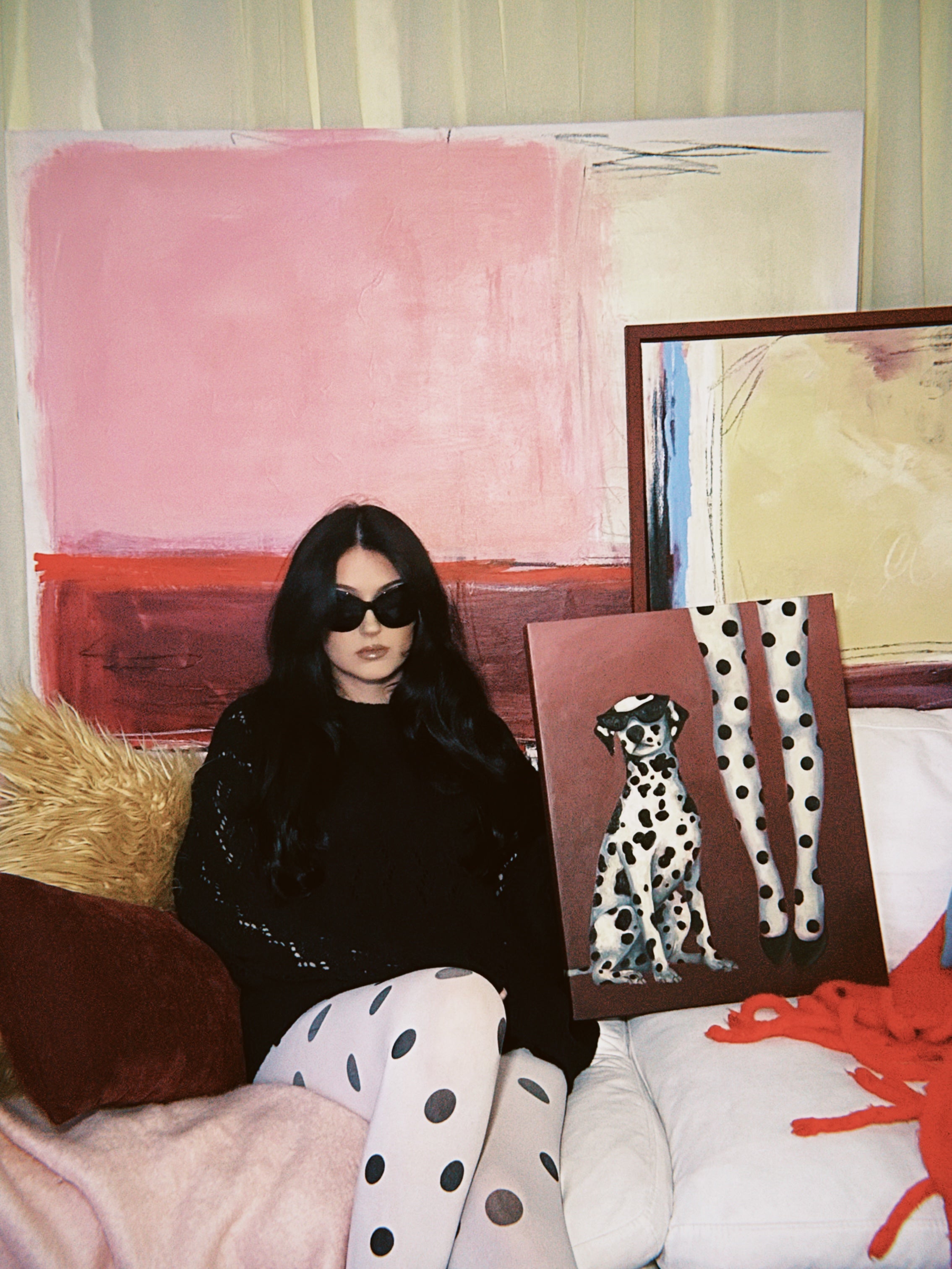 Girl wearing polka dot tights sitting on a couch with abstract art behind her, and a Dalmatian painting.